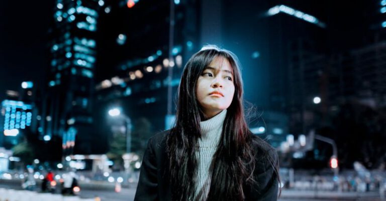 Outdoor Lighting - Brunette Girl Sitting on Bench in City Street at Night